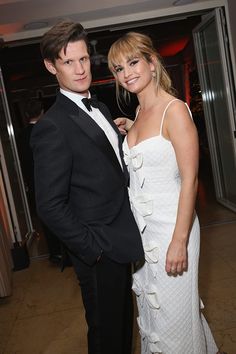 two people standing next to each other in formal wear at an event, one wearing a tuxedo and the other wears a white dress