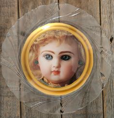 an old doll with blue eyes is in a glass plate on a wooden table top