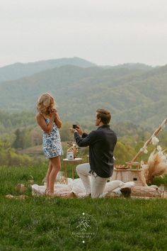 a man and woman are sitting on the grass in front of an outdoor picnic table