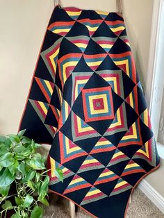 a black and red quilt sitting on top of a wooden chair next to a potted plant