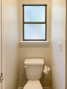 a white toilet sitting under a window in a bathroom