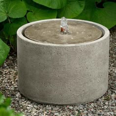 a concrete water fountain surrounded by gravel and plants