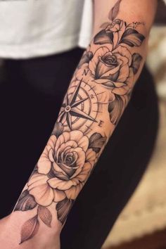 a woman's arm with roses and compass tattoo on it