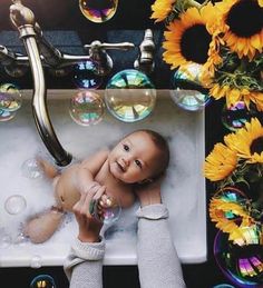 a baby sitting in a sink surrounded by soap bubbles and sunflowers