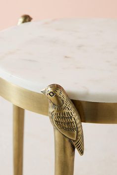 a gold bird figurine sitting on top of a marble and brass coffee table