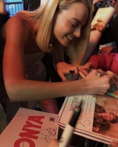 a woman is signing autographs for children at a table with other people and magazines