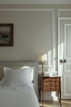 a bed with white sheets and pillows next to a painting on the wall above it