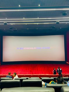 people sitting in chairs watching a movie on a large screen at the front of an auditorium