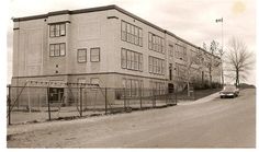 an old photo of a large building with cars parked in front of it and fenced off area