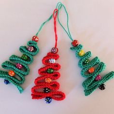 three crocheted christmas tree ornaments hanging from strings on a white surface with beads