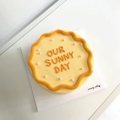 a yellow cake with the words our sunny day on it sitting on top of a piece of paper