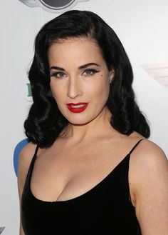 a woman with dark hair and red lipstick wearing a black dress on the red carpet