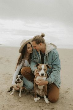 a man and woman are sitting on the beach with their two dogs, one brown and white