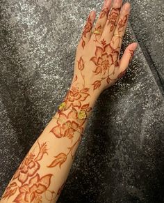 a woman's hand with henna tattoos on her arm and the wrist is decorated with flowers