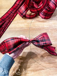 someone is tying a red and black plaid bow to a piece of fabric on a wooden table