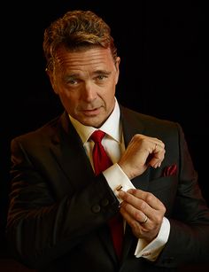 a man in a suit and red tie is posing for the camera with his hands on his chest