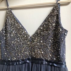 a blue dress with gold sequins is hanging on a hanger in front of a white wall