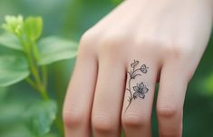 a woman's hand with a small flower tattoo on her left ring and the other half of her finger