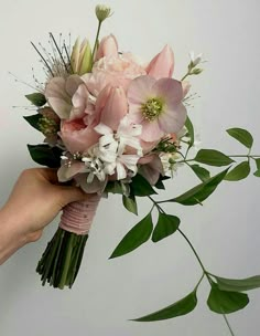 a hand holding a bouquet of flowers on a white background with greenery in the foreground