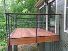 a wooden deck with metal railings on the side of a house next to trees