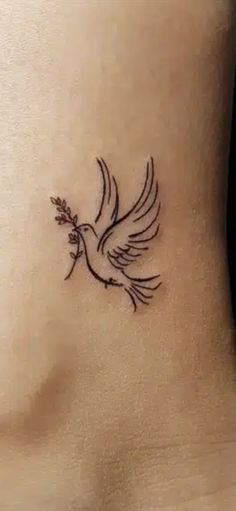 a small bird tattoo on the side of a woman's stomach, with an olive branch in its beak