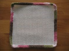 a square dishcloth with pink, green and white designs on it sitting on a wooden surface