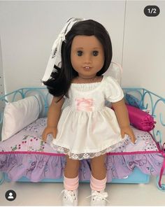 a doll sitting on top of a bed next to a pink pillow and white shoes