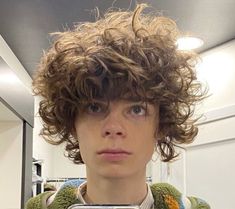 a man with curly hair taking a selfie in front of a mirror while wearing a sweater