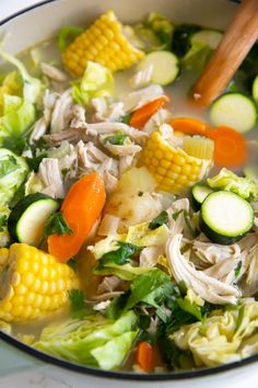 a bowl filled with soup and vegetables on top of a white countertop next to a wooden spoon