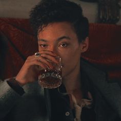 a man sitting on a couch drinking from a glass in front of his face and looking at the camera