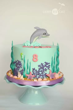 a birthday cake with a dolphin on top and under the sea theme is decorated in pastel colors