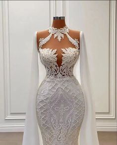 a white wedding dress with long sleeves and lace detailing on the neckline is displayed in front of a mannequin