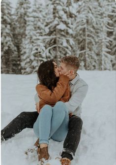 a man and woman sitting in the snow with their arms around each other as they kiss