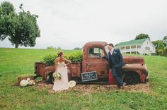 a bride and groom standing next to an old truck in a field with pumpkins