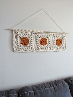 a white crocheted wall hanging with three orange flowers on it's side