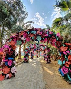 an archway decorated with colorful paper flowers and palm trees on the side of a road