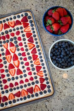 a cake with strawberries and blueberries on it next to a bowl of berries