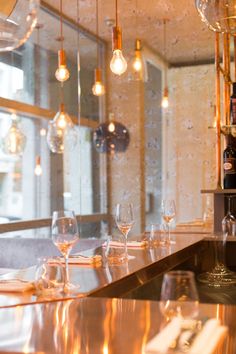 wine glasses are lined up on the bar in front of an open window with hanging lights