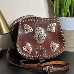 Handmade Vintage Brown Leather With Metal Studs Shoulder Handbag With Silver Tone Hardware And Hamsa Detail With Orange Gemstones. Main Compartment Raw Suede Lining Zip Pocket Under Flap Distressed Aged Leather To Give It A Worn In Western Style Look Height 9” Width 11” Depth 2.5” Strap Drop 21” Bag Dimensions Are Based On Approximate Measurements Photos Are The Best Descriptors. Tags: Gypsy, Boho, Bohemian, 60s, 70s, Retro, Saddle Bag, Leather, Distressed, Western, Moroccan, Hamsa, Faerie, Fair Artisan Crossbody Saddle Bag, Red Leather Festival Bag, Orange Bags With Palladium Hardware, Rectangular Orange Shoulder Bag With Palladium Hardware, Orange Leather Shoulder Bag With Palladium Hardware, Vintage Orange Leather Bags, Bohemian Orange Crossbody Shoulder Bag, Retro Vintage Brown Hand Tooled Shoulder Bag, Vintage Hand-tooled Rectangular Saddle Bag