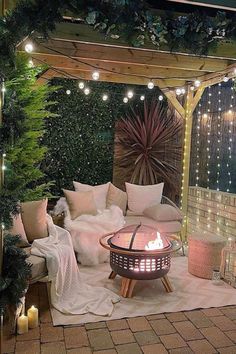 a fire pit surrounded by greenery and lights in a patio area with white pillows