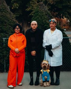 three people and a dog posing for a photo in front of a fence with trees