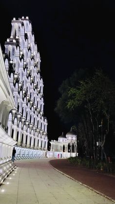 a large white building sitting next to a park at night with lights on it's sides