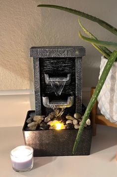 a candle is lit next to a water fountain with rocks and stones around it on a table