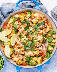 a blue skillet filled with chicken, broccoli and other vegetables next to limes