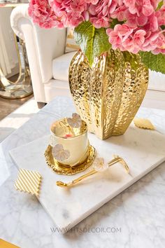 pink flowers are in a gold vase on a marble tray next to a cup and saucer