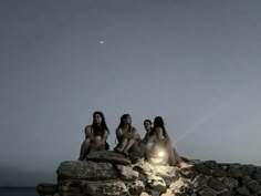 three women sitting on rocks in front of the ocean at night with their lights on