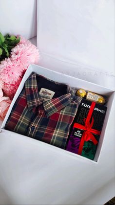 an open white box containing a plaid shirt, tie and pink carnations next to a bouquet of flowers