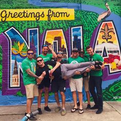 a group of young men standing in front of a wall with the words greetings from new orleans painted on it