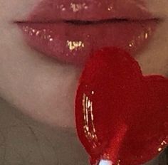 a woman's lips are covered with shiny lipstick and a heart shaped lollipop