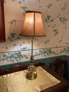 a table with a lamp on top of it next to a wallpapered wall